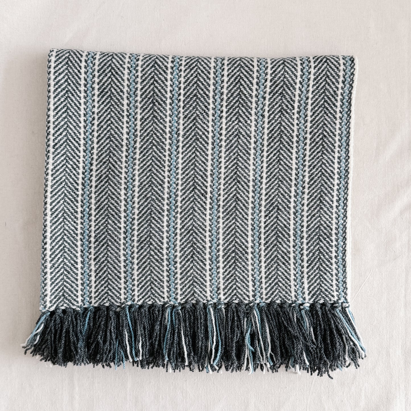 Textured blanket with herringbone pattern, natural indigo dye colours and fringes on a light background