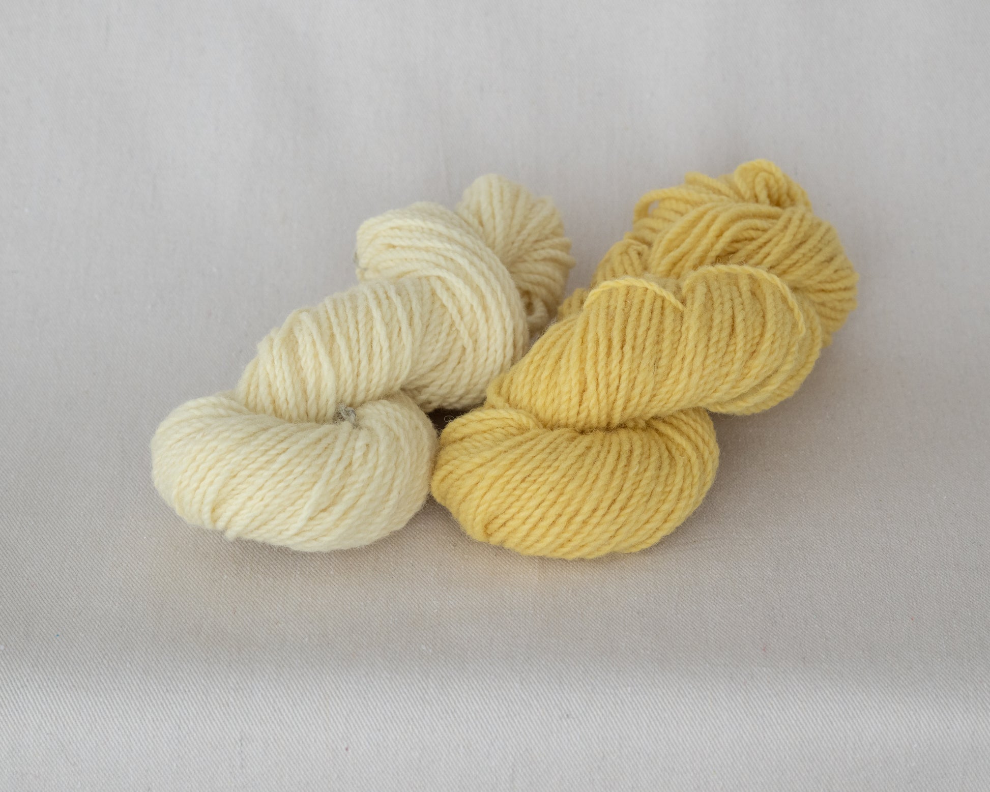 Two skeins of yarn, one cream and one yellow, on a light gray background.