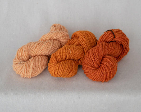 Three skeins of yarn in peach, orange, and red on a light gray background