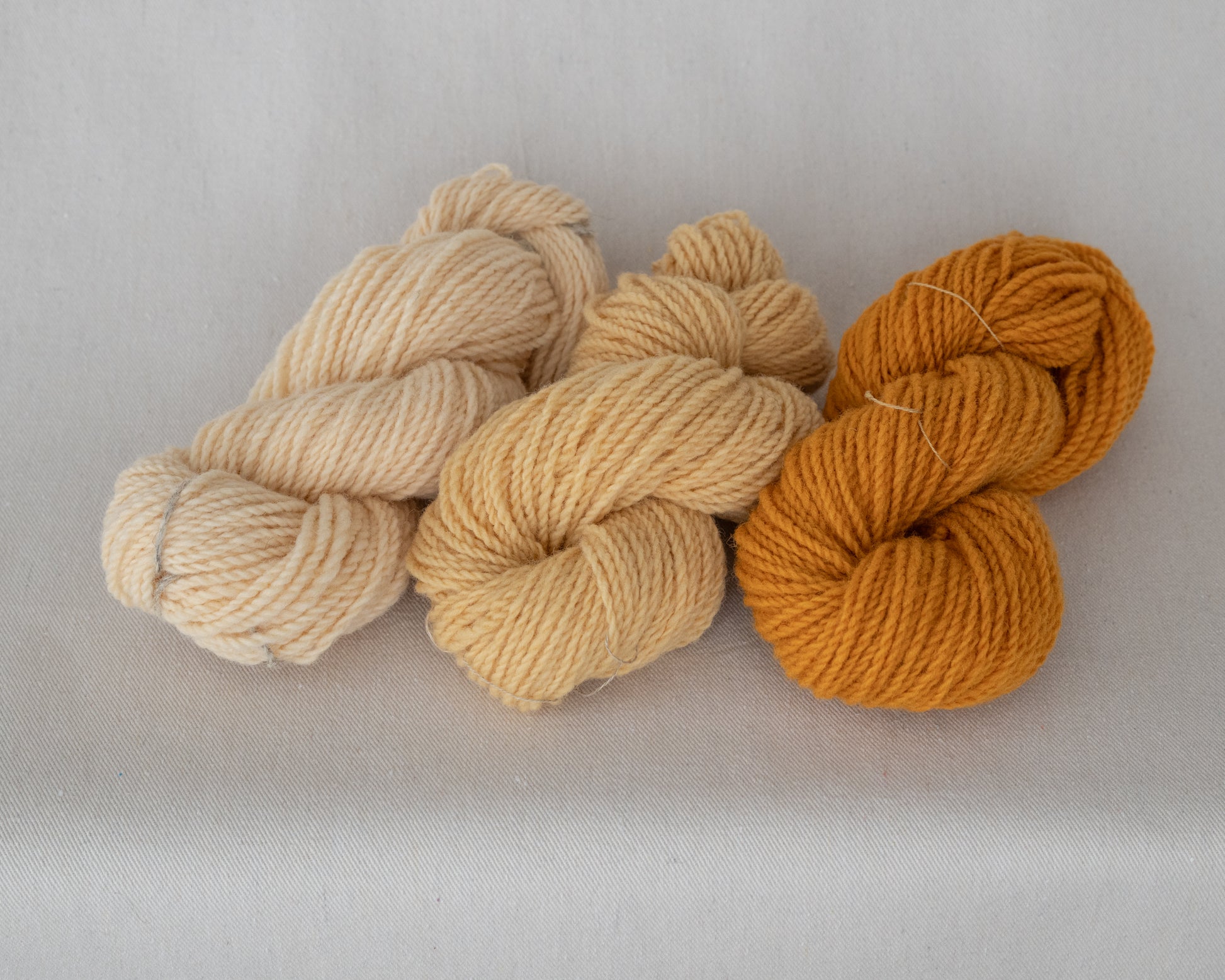 Three skeins of yarn in beige, brown, and orange on a light gray background