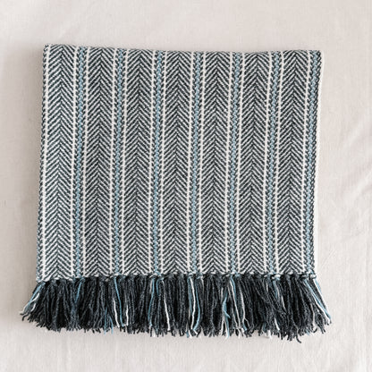 Textured blanket with herringbone pattern, natural indigo dye colours and fringes on a light background