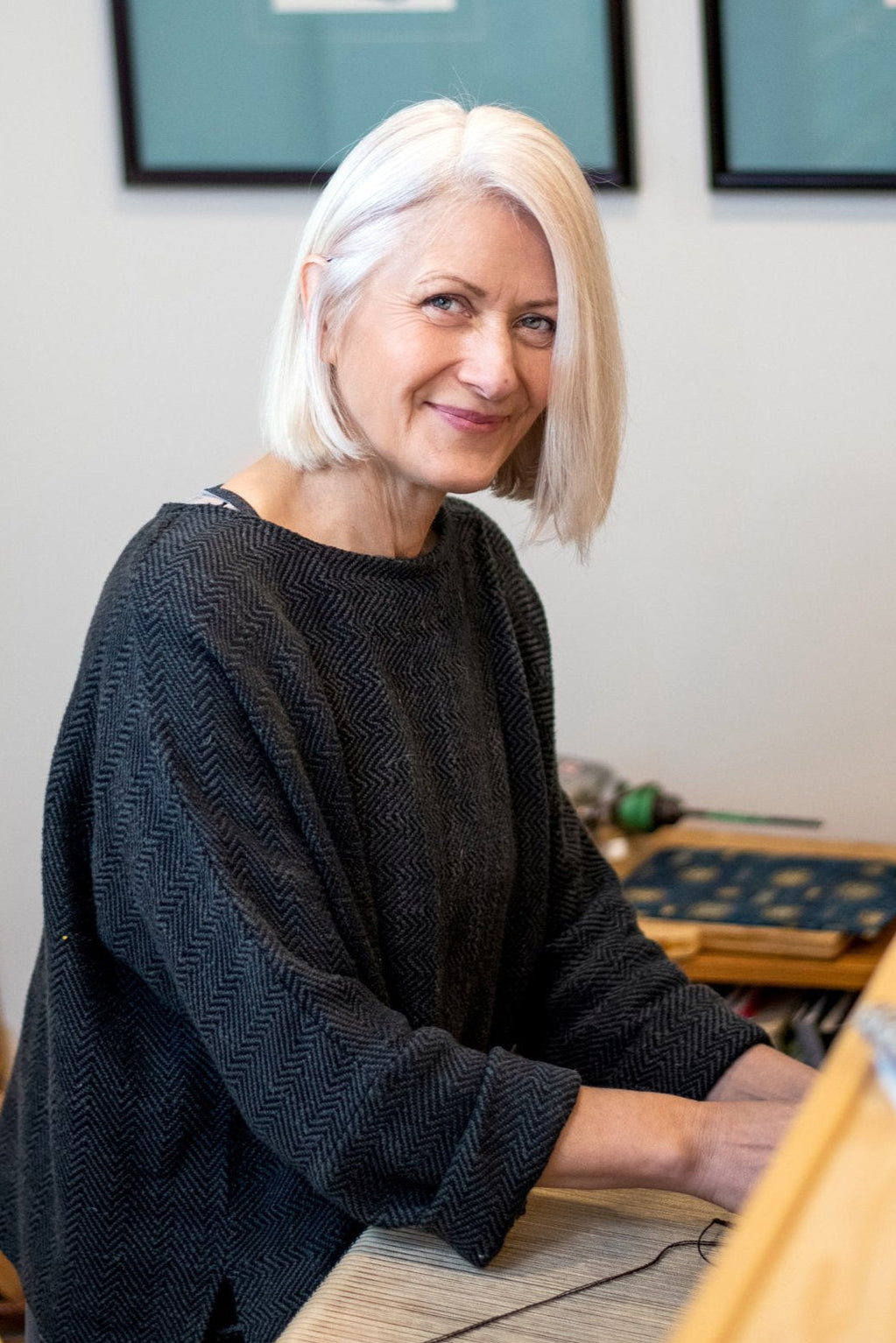 Woman sitting at a loom with artwork in the background